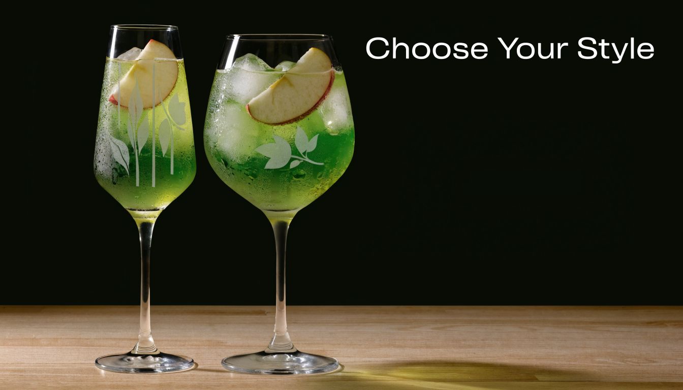 Two elegant glasses filled with a green cocktail and apple slices, sitting on a wooden surface.